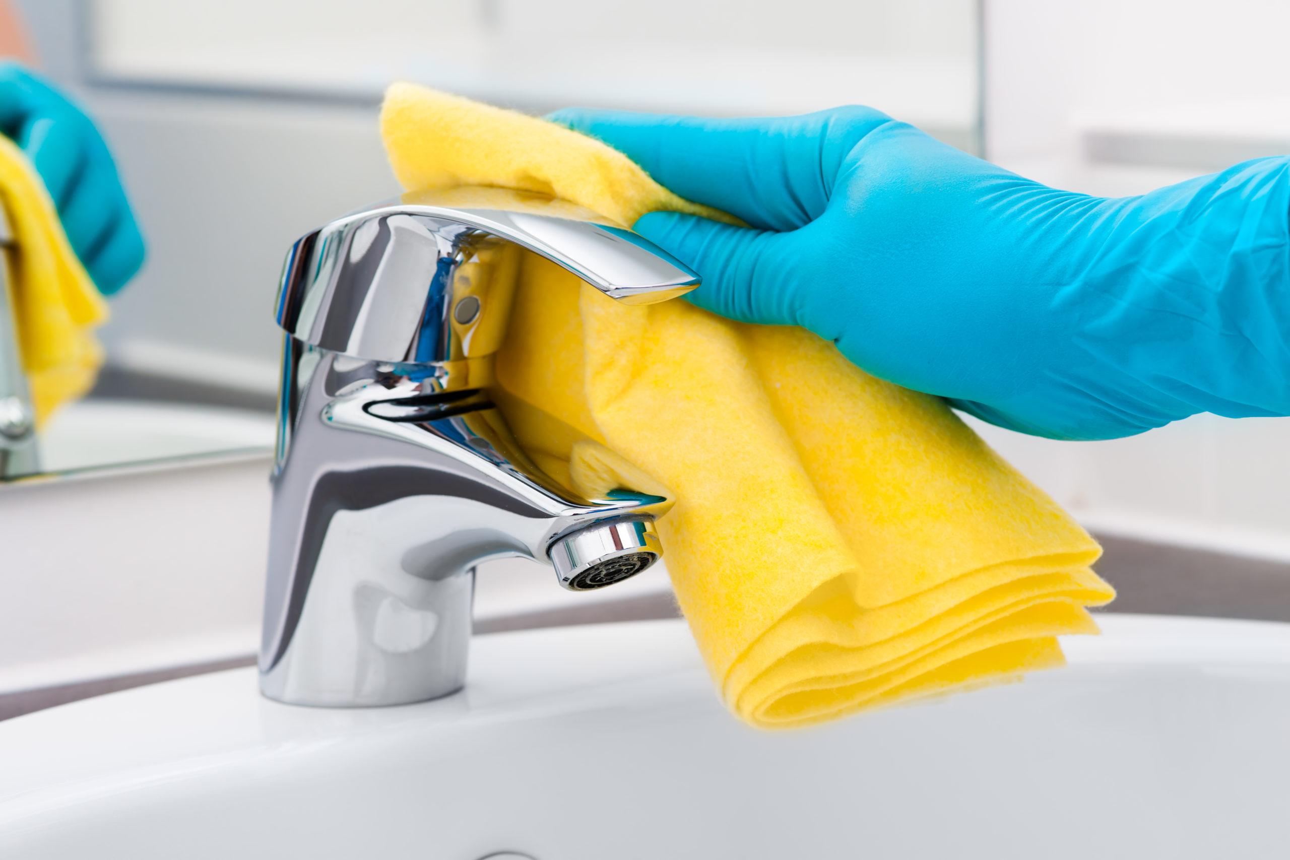 gloved hand wipes the faucet with a yellow cloth